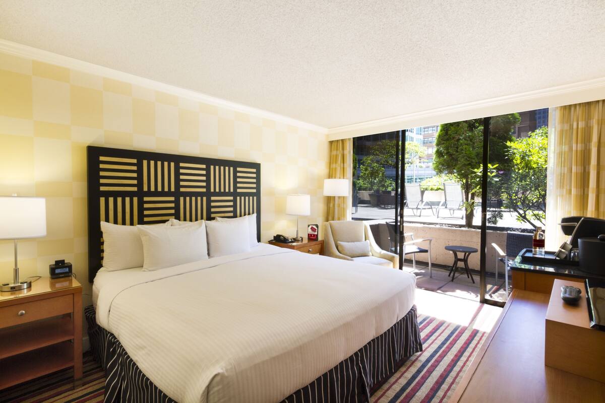 A hotel room with a large bed, a desk, a chair, and a view of the outdoors.