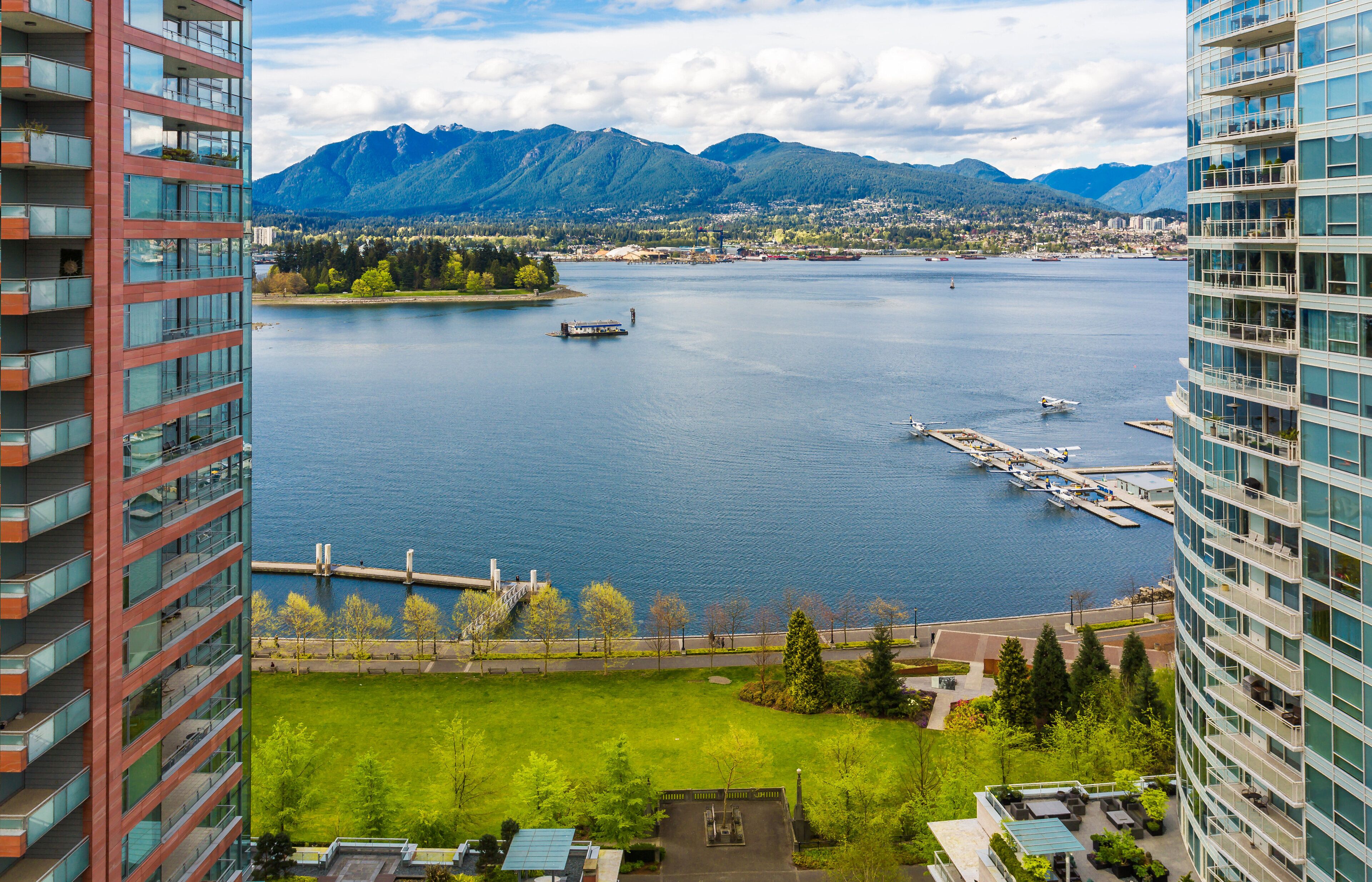 A high-rise hotel overlooking a lake with boats, a dock, and mountains in the background.