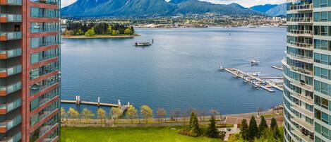 A high-rise hotel overlooking a lake with boats, a dock, and mountains in the background.