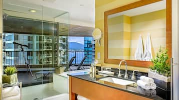 A modern bathroom with a glass-enclosed shower, a large mirror, and a view of the cityscape.