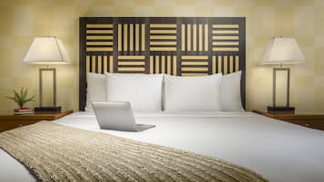 Una cama bien hecha con una computadora portátil, dos lámparas de noche y un cabecero estampado.