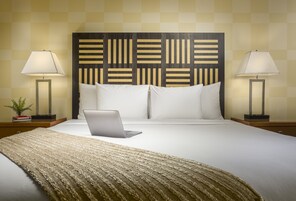Una cama bien hecha con una computadora portátil, dos lámparas de noche y un cabecero estampado.