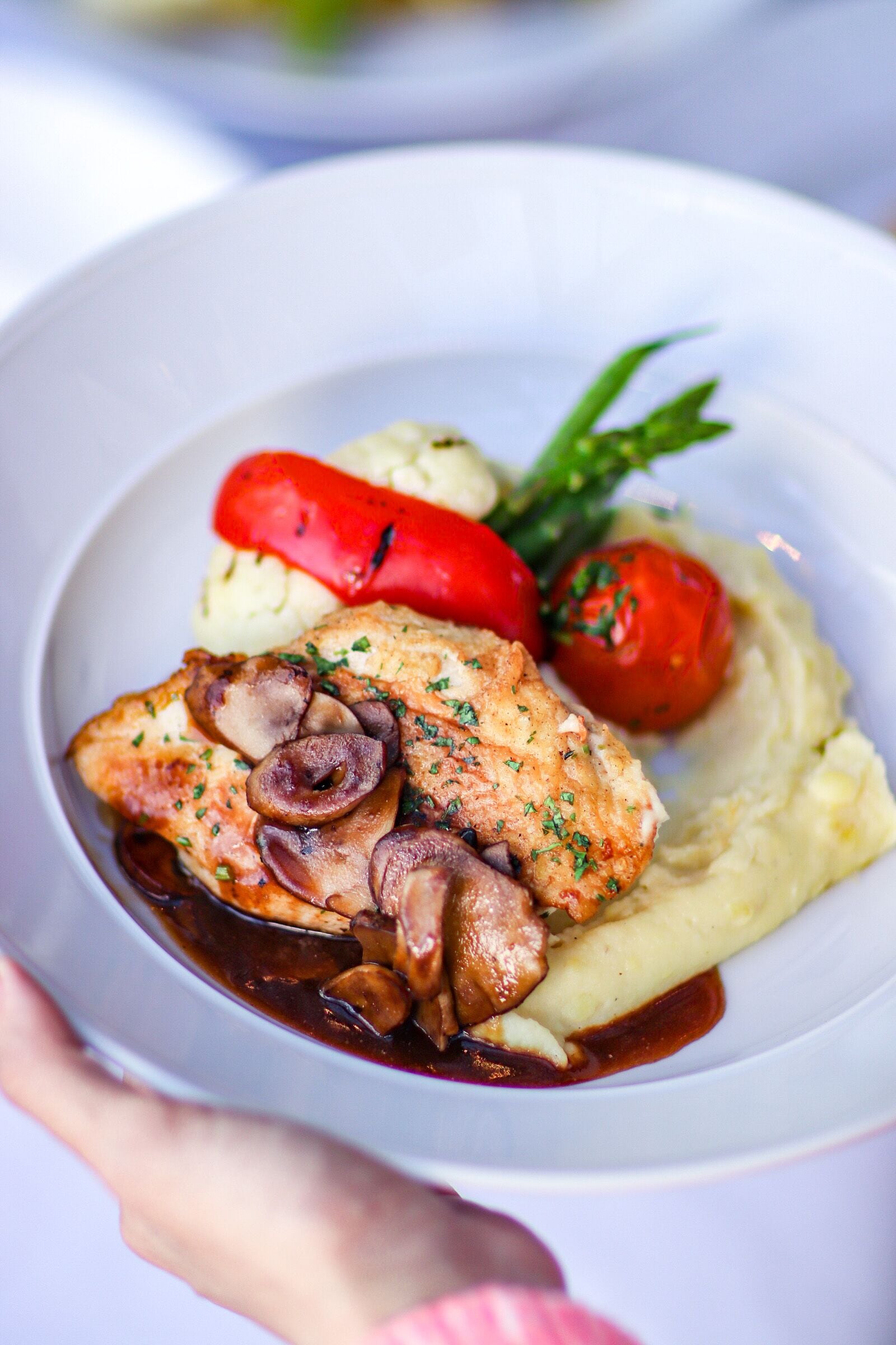 A plate with a piece of chicken, mushrooms, mashed potatoes, and cherry tomatoes.