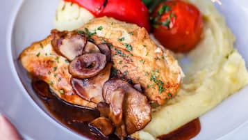 A plate with a piece of chicken, mushrooms, mashed potatoes, and cherry tomatoes.