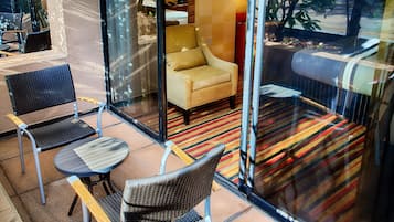 A modern hotel lobby with a glass partition, wicker chairs, a small round table, and a striped rug.