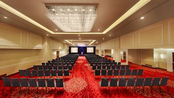 A conference room with rows of black chairs, a red carpet, and a large chandelier.