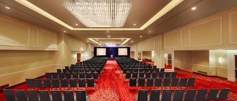 Un salón de conferencias con filas de sillas negras, una alfombra roja y una gran lámpara de araña.