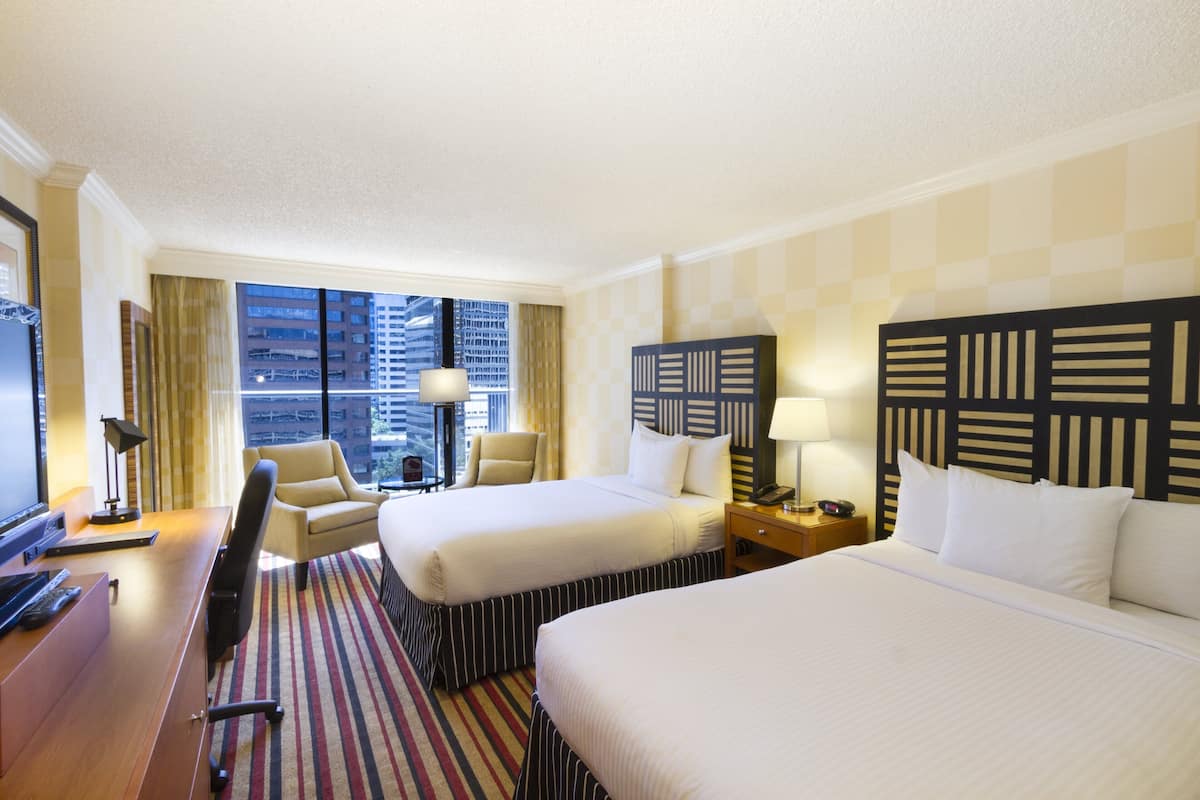 A hotel room with two beds, a desk with a computer, a chair, a TV, and a window with a city view.