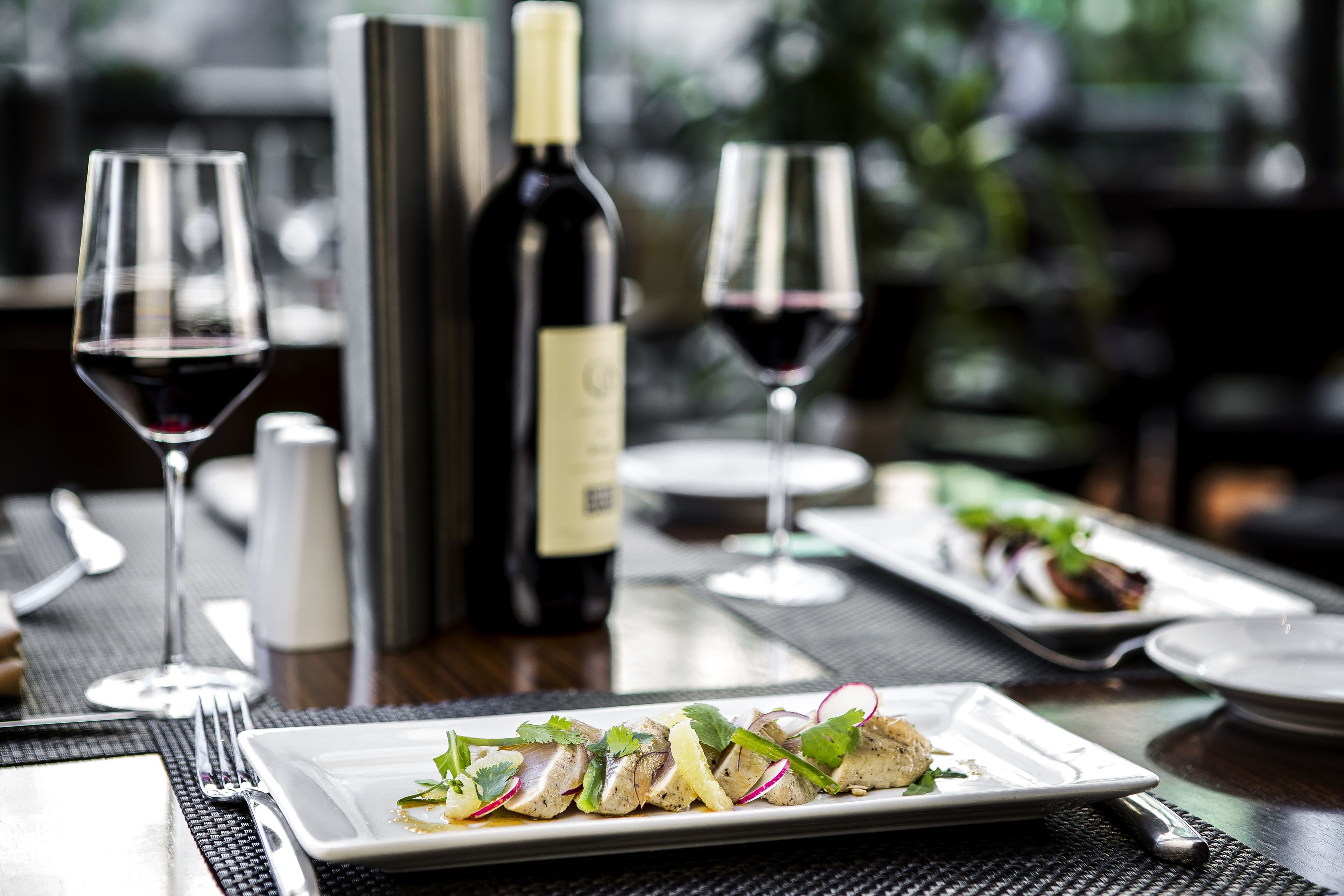A dining table set with plates of food, wine glasses, and a bottle of wine.
