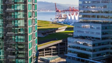 A modern high-rise building with a glass facade, a rooftop garden, and a view of the waterfront with cranes.