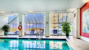 Piscina interna com vista clara para montanhas, cadeiras de sol e plantas em vasos.
