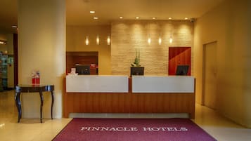 A reception desk with a wooden finish and a glass partition, a red carpet with "Pinnacle Hotels" text, and a textured wall behind the desk.