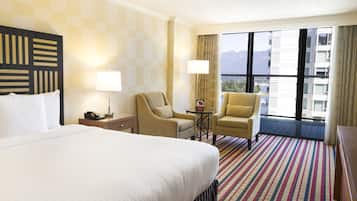 Habitación de hotel con una cama grande, dos sillones, una mesita y vistas a las montañas por la ventana.