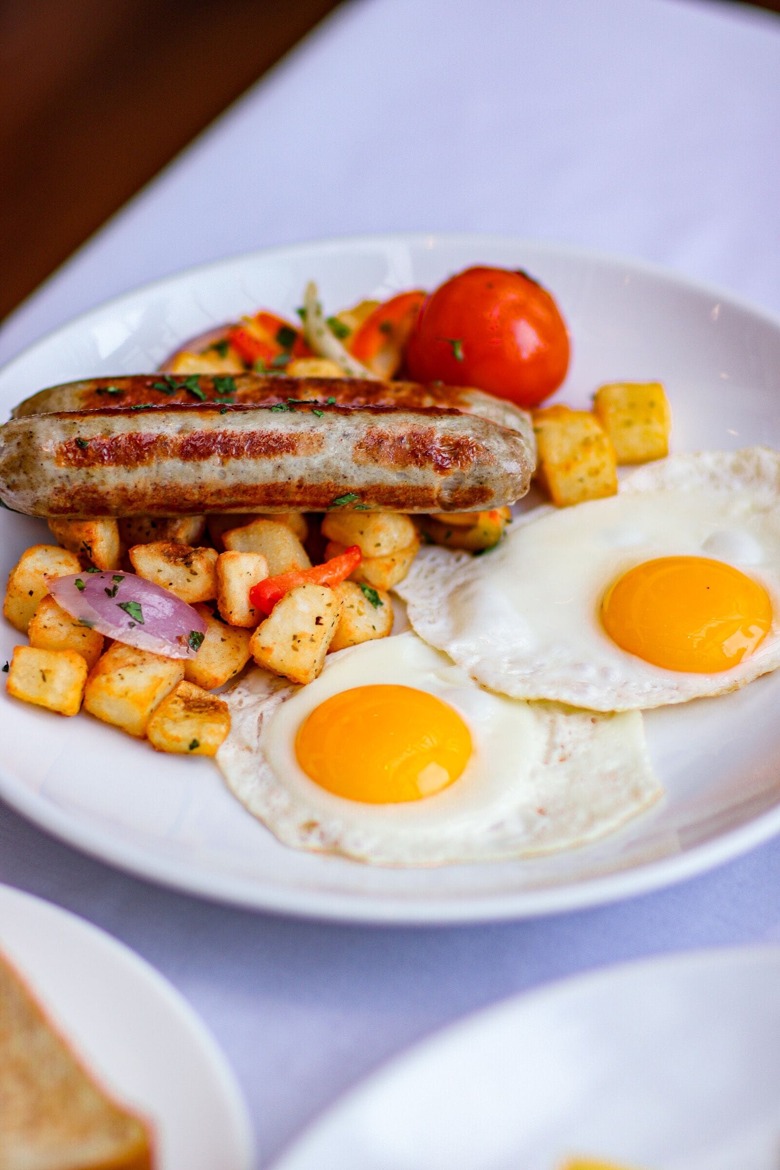 A plate with two fried eggs, sausages, and diced potatoes.