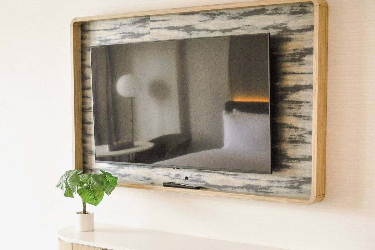 A flat-screen TV mounted on a wall with a distressed wood frame, a small potted plant, and a wooden console below.