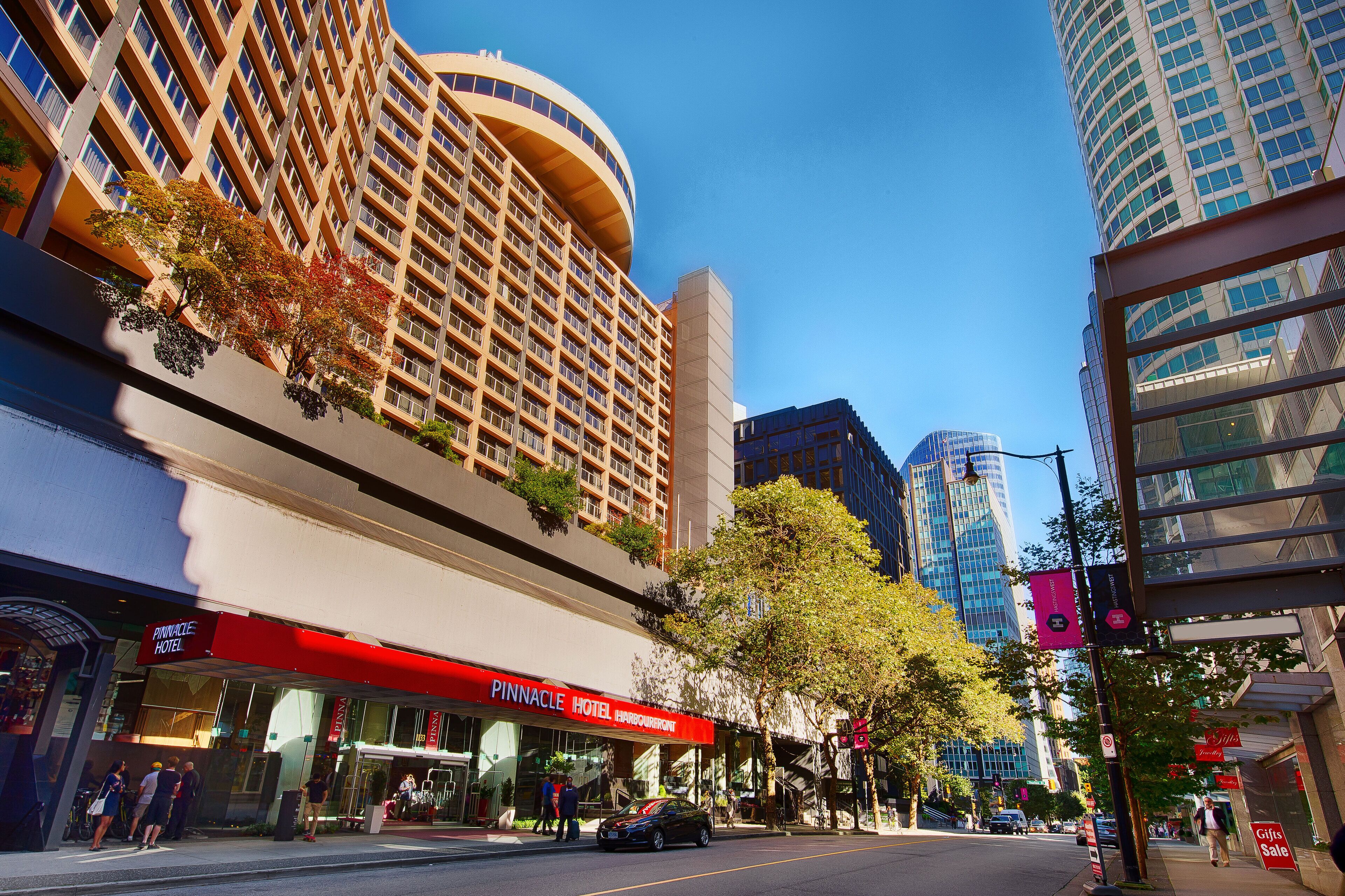 A hotel with a red awning, a large tree, and modern high-rise buildings in the background.