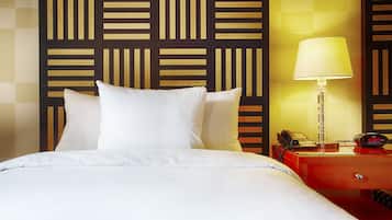 A hotel room with a bed, pillows, a bedside table with a lamp, a phone, and a wall with a geometric pattern.