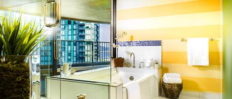 A modern bathroom with a glass shower enclosure, a large bathtub, and a view of a cityscape through the window.