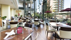 Um restaurante moderno com várias mesas e cadeiras, janelas amplas e área externa com guarda-sóis.
