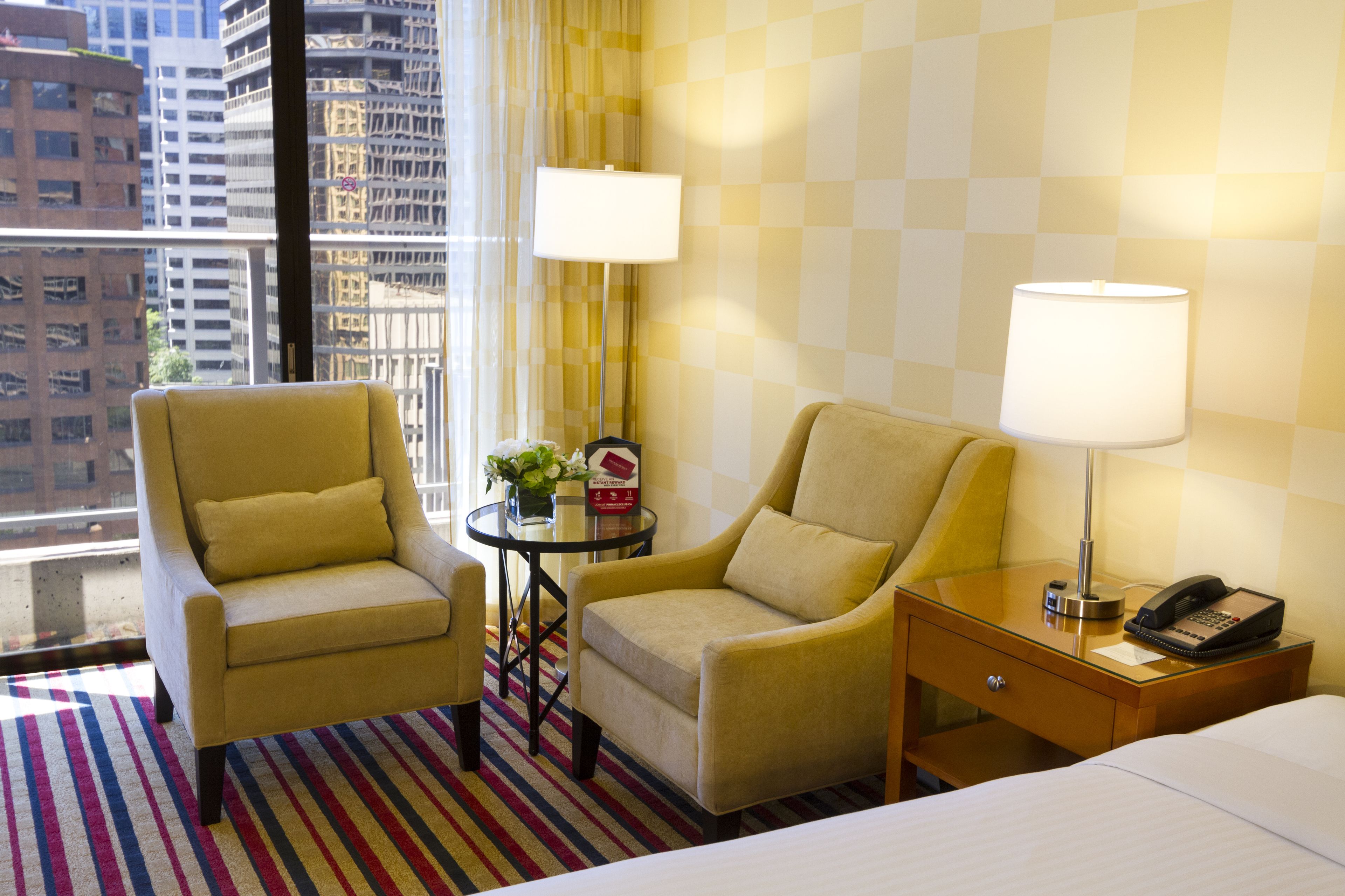 Habitación de hotel con dos sillones, una mesita con lámpara, una mesita de noche con teléfono y una cama.