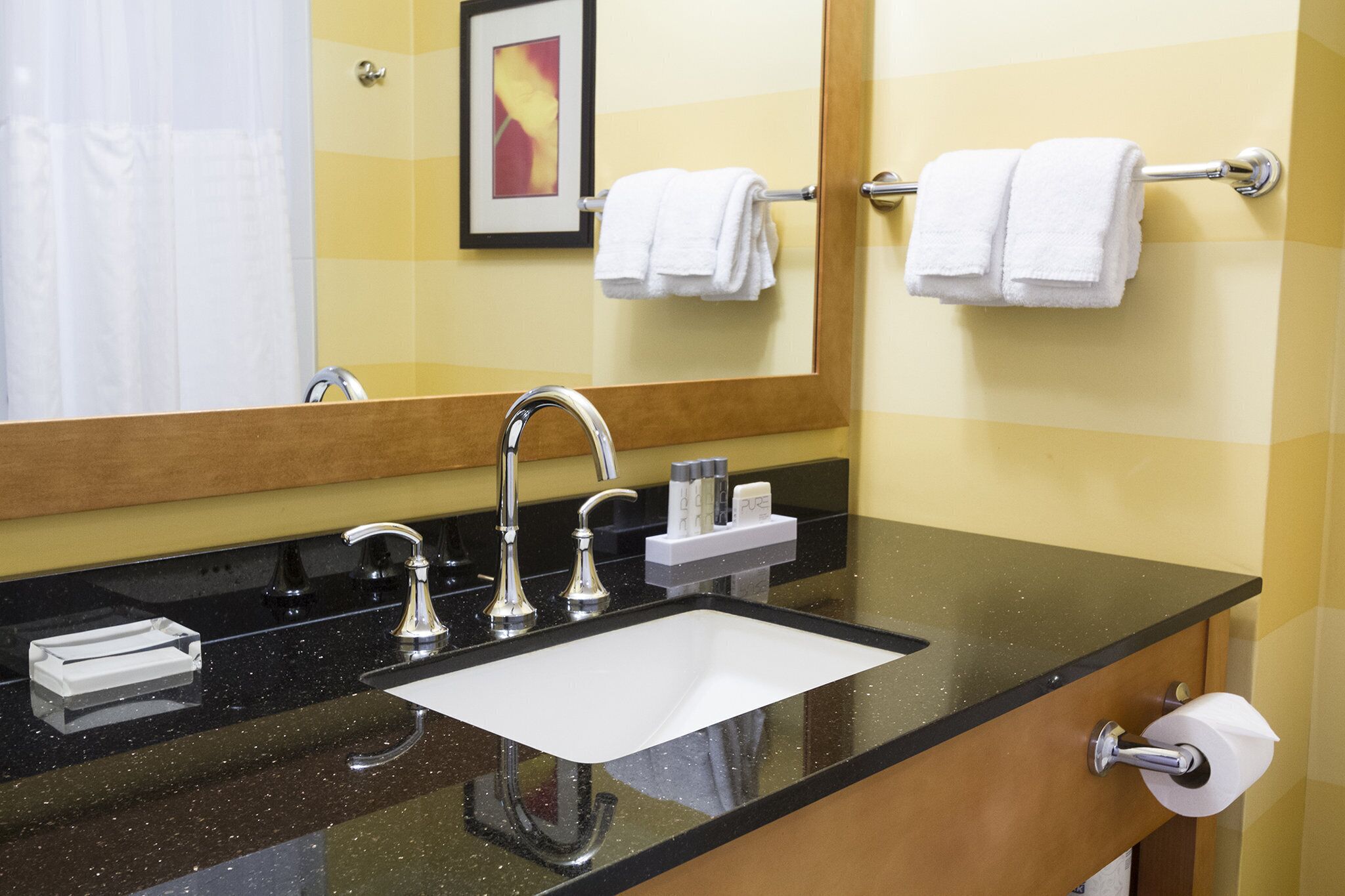 A bathroom with a black countertop, a white sink, and two towel bars with white towels.
