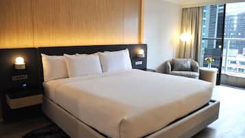 A hotel room with a large bed, bedside lamps, a chair, and a window with a city view.