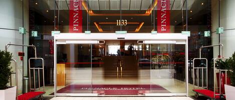 The entrance to the Pinnacle Hotel with a glass facade, a red carpet, and a visible elevator.