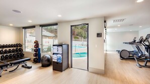 A gym with exercise equipment, a bench, dumbbells, and a basket of towels. - DoubleTree by Hilton Pomona (Pomona)
