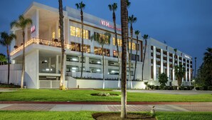 A modern hotel with a VITA sign, multiple floors, and a well-maintained lawn with palm trees. - DoubleTree by Hilton Pomona (Pomona)