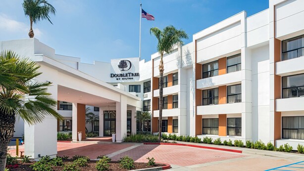 A modern hotel with a white facade, palm trees, and an American flag. - DoubleTree by Hilton Pomona (Pomona)