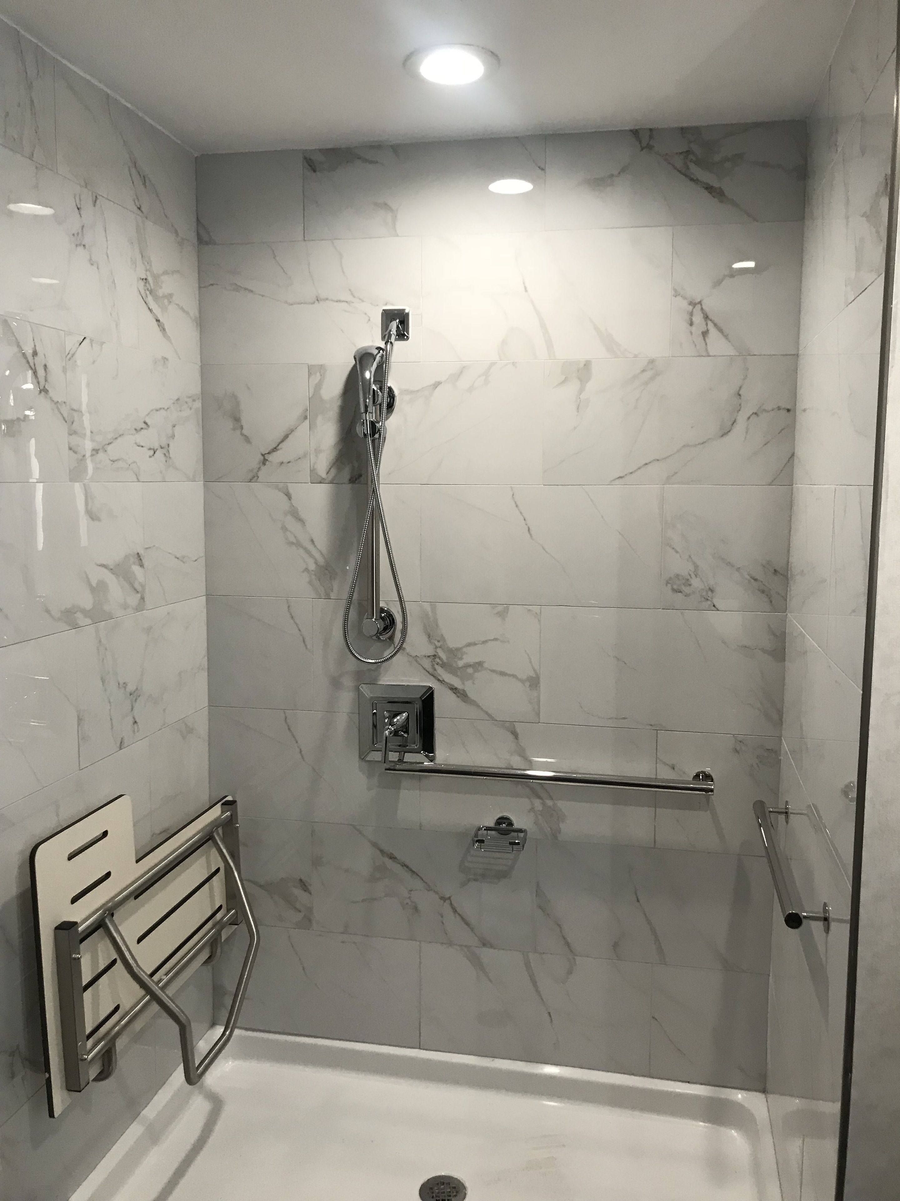 Un baño moderno con cabina de ducha a ras de suelo, baldosas de mármol, un cabezal de ducha manual y un accesorio de ducha manual, un perchero y un cerramiento de vidrio para la ducha.