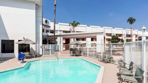 A swimming pool with lounge chairs and umbrellas, surrounded by a white fence, and a building with a sign that reads "DoubleTree". - DoubleTree by Hilton Pomona (Pomona)