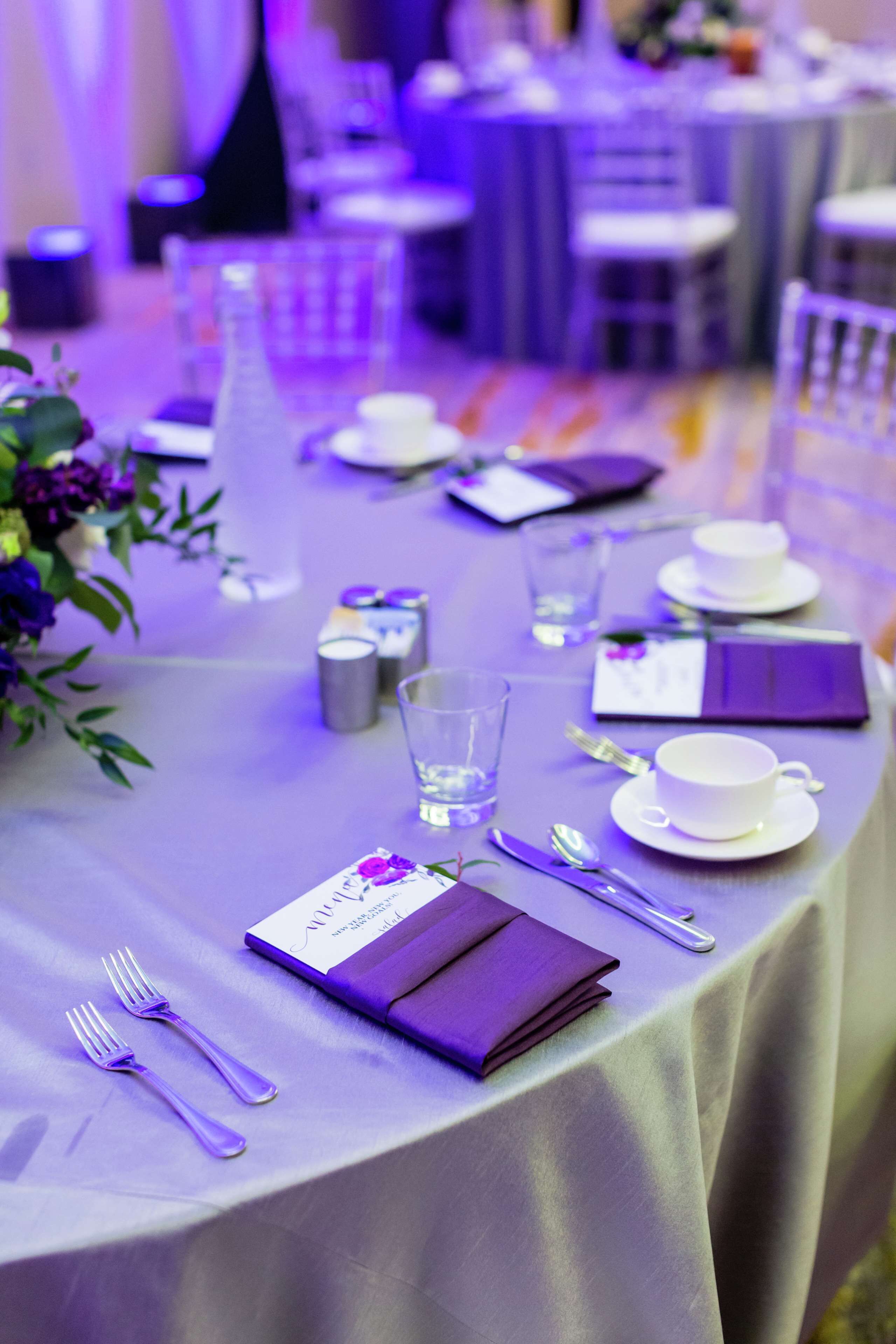 A table set with white plates, silverware, and a purple menu.