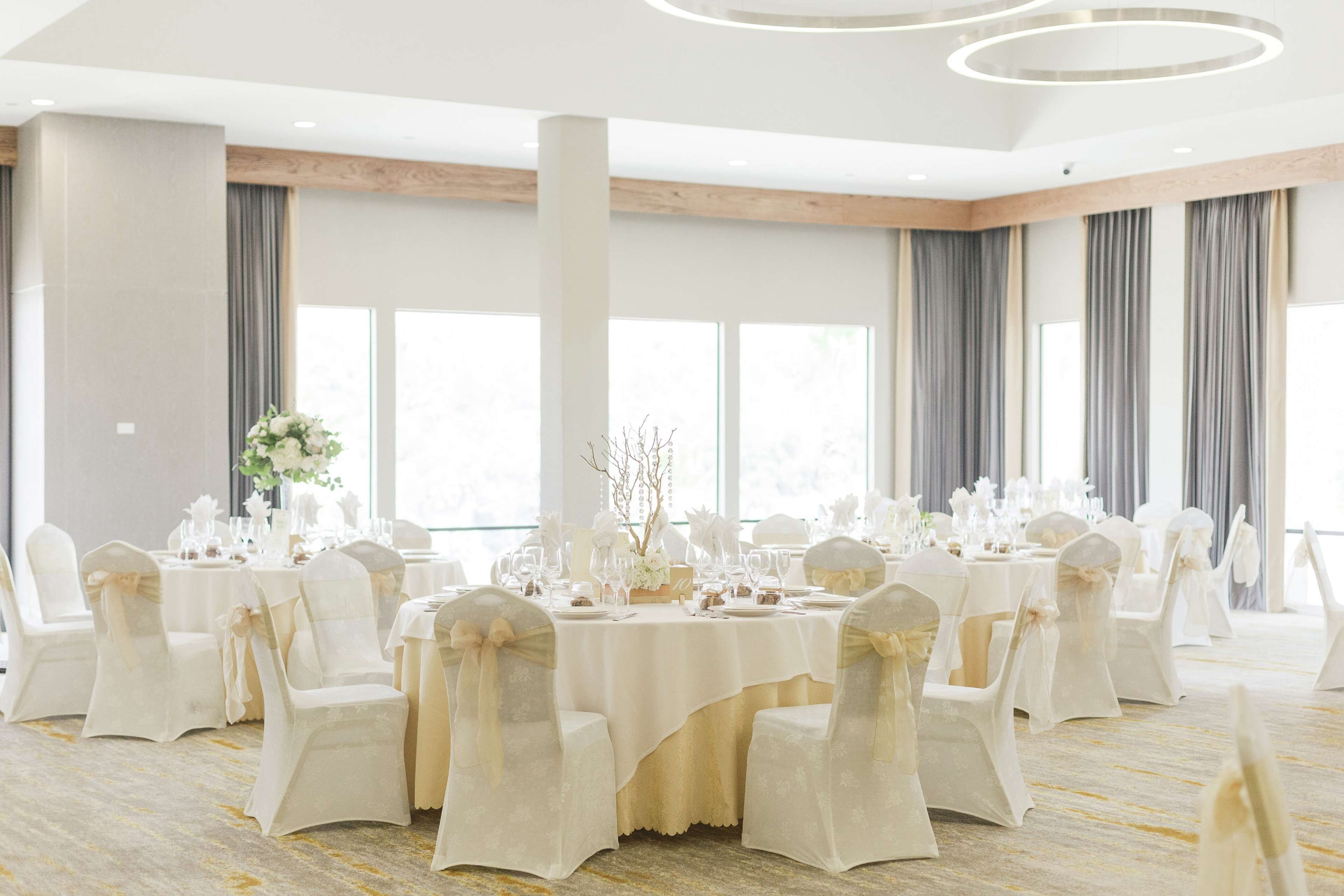 Un salón de banquetes con mesas redondas, sillas blancas y una paleta de colores neutros.