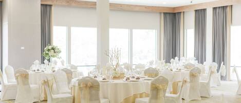 Un salón de banquetes con mesas redondas, sillas blancas y una paleta de colores neutros.