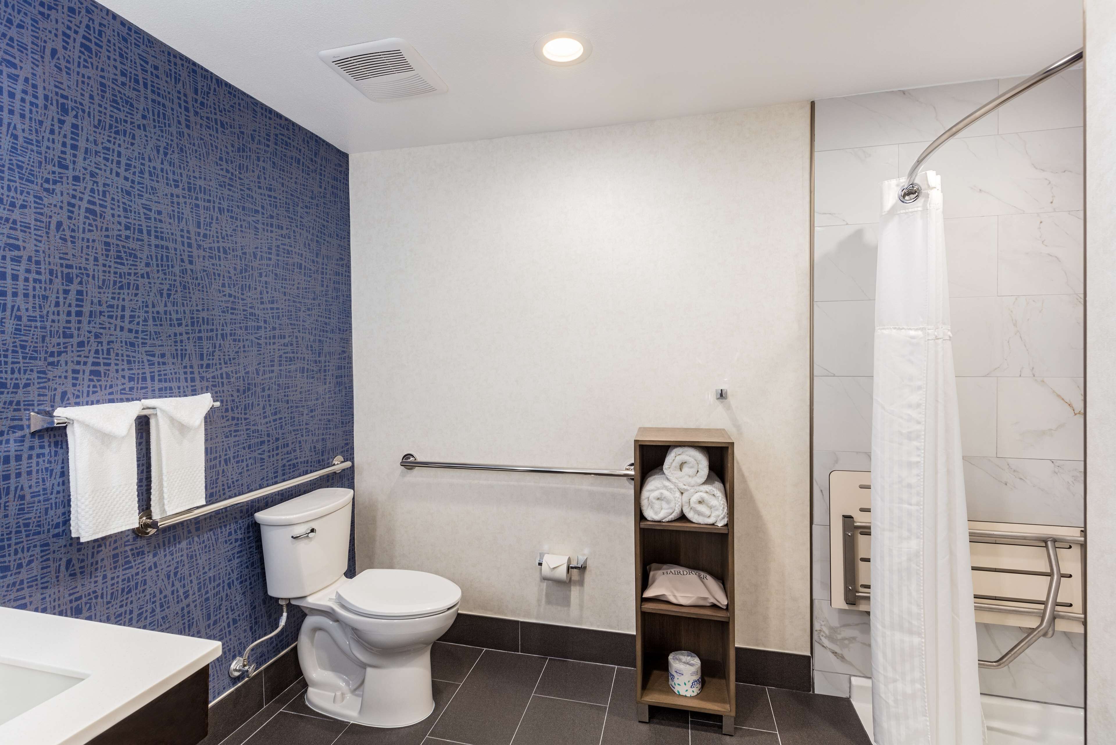 Ein modernes Badezimmer mit blauer Mosaikwand, Toilette in Weiß, Dusche mit Glastür und Ablage mit Handtüchern.