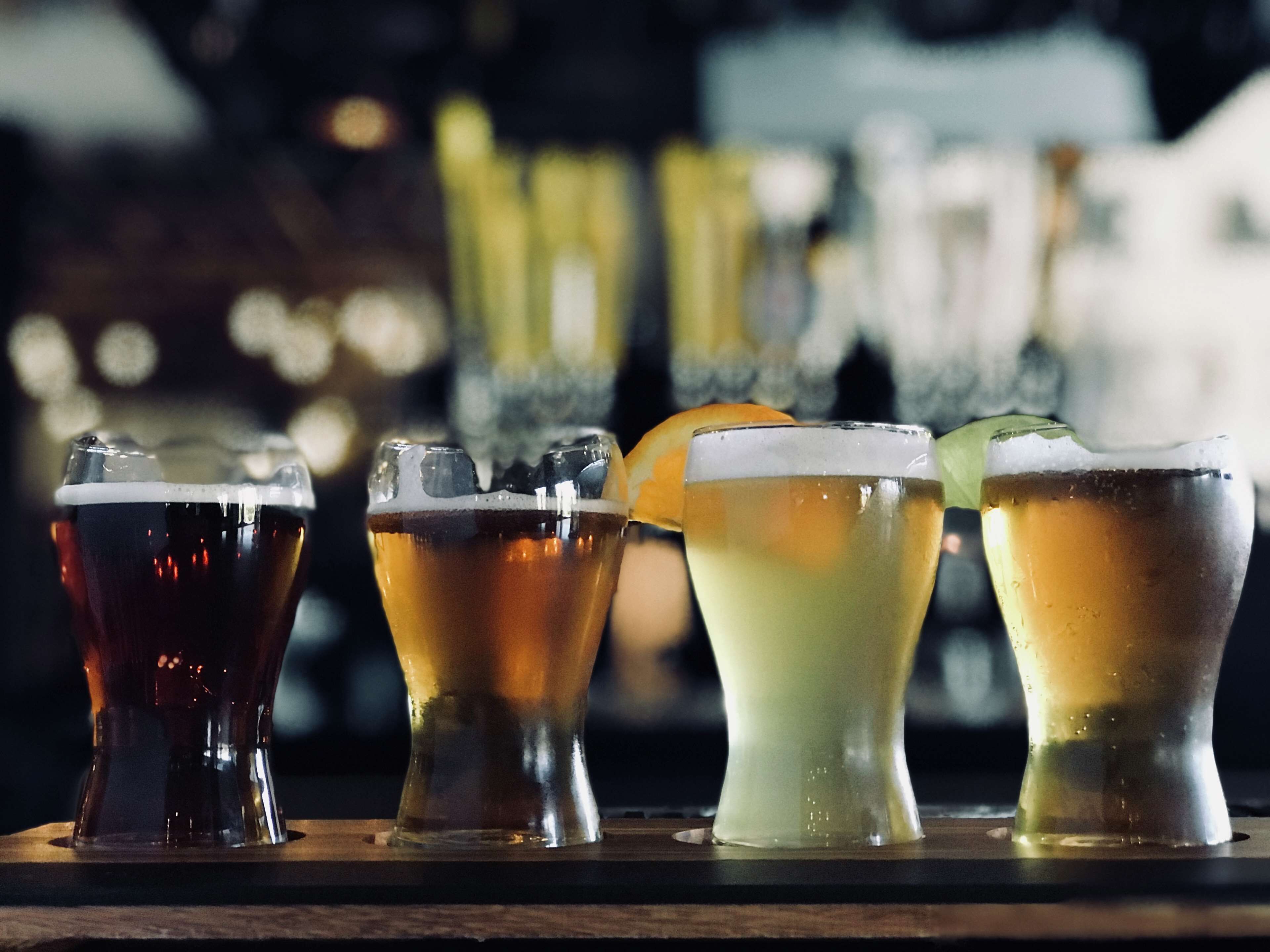 Four glasses of different beverages on a bar counter.