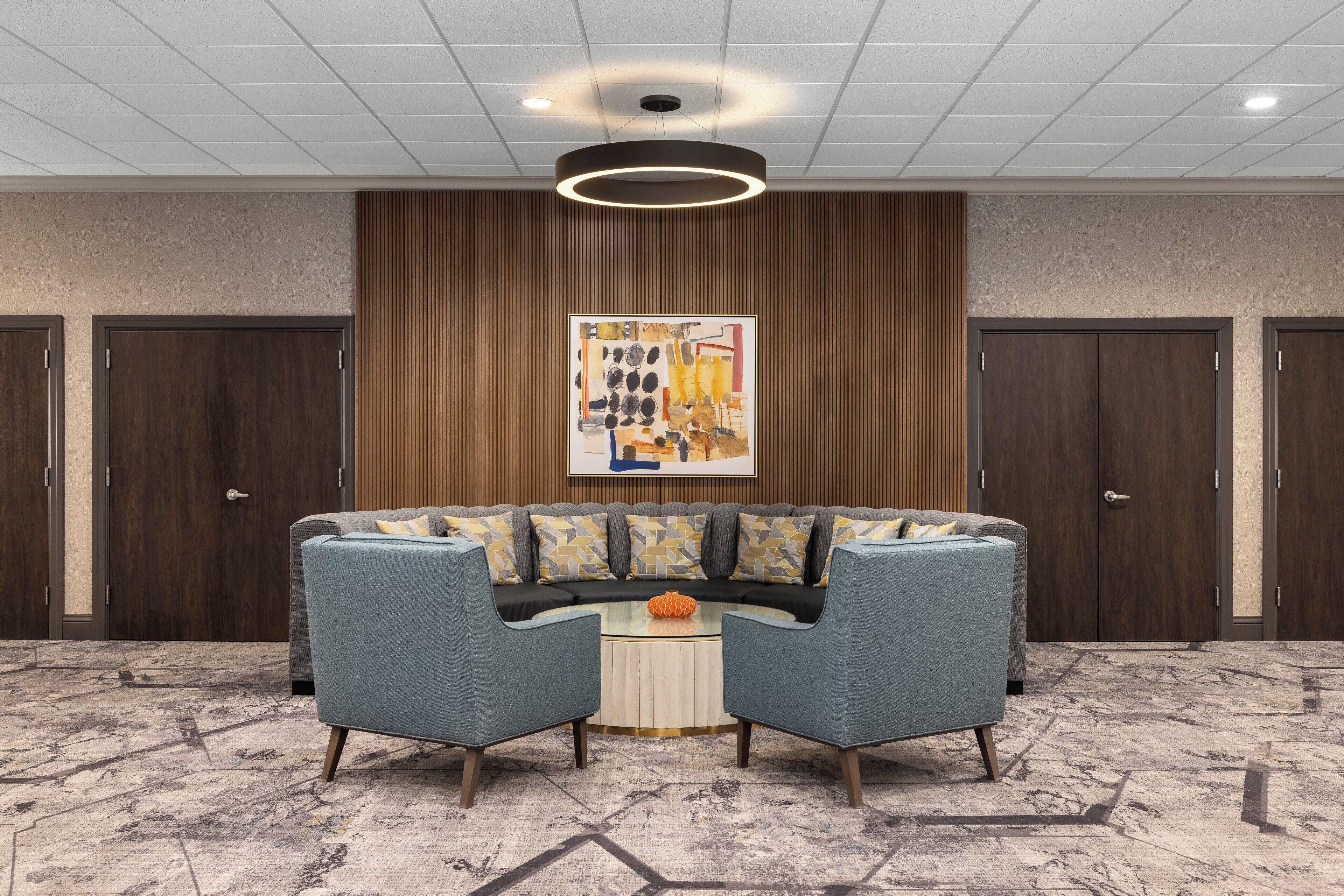 A lobby with a sectional sofa, a round coffee table, and a large abstract painting on the wall.