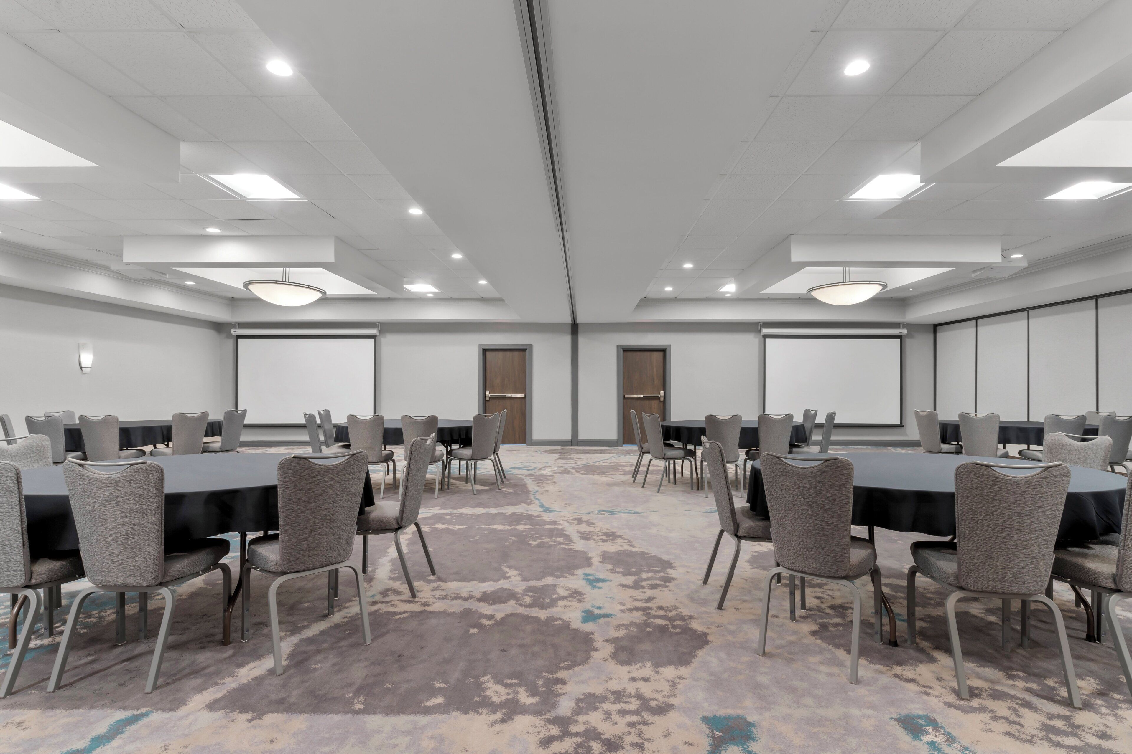 A conference room with multiple tables and chairs, a carpeted floor, and a white ceiling with recessed lighting.