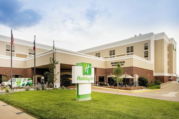 Um hotel Holiday Inn com fachada de tijolos, uma placa verde e um mastro com a bandeira americana.