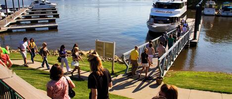 A waterfront promenade with people walking, a dock with boats, and a clear view of the water.