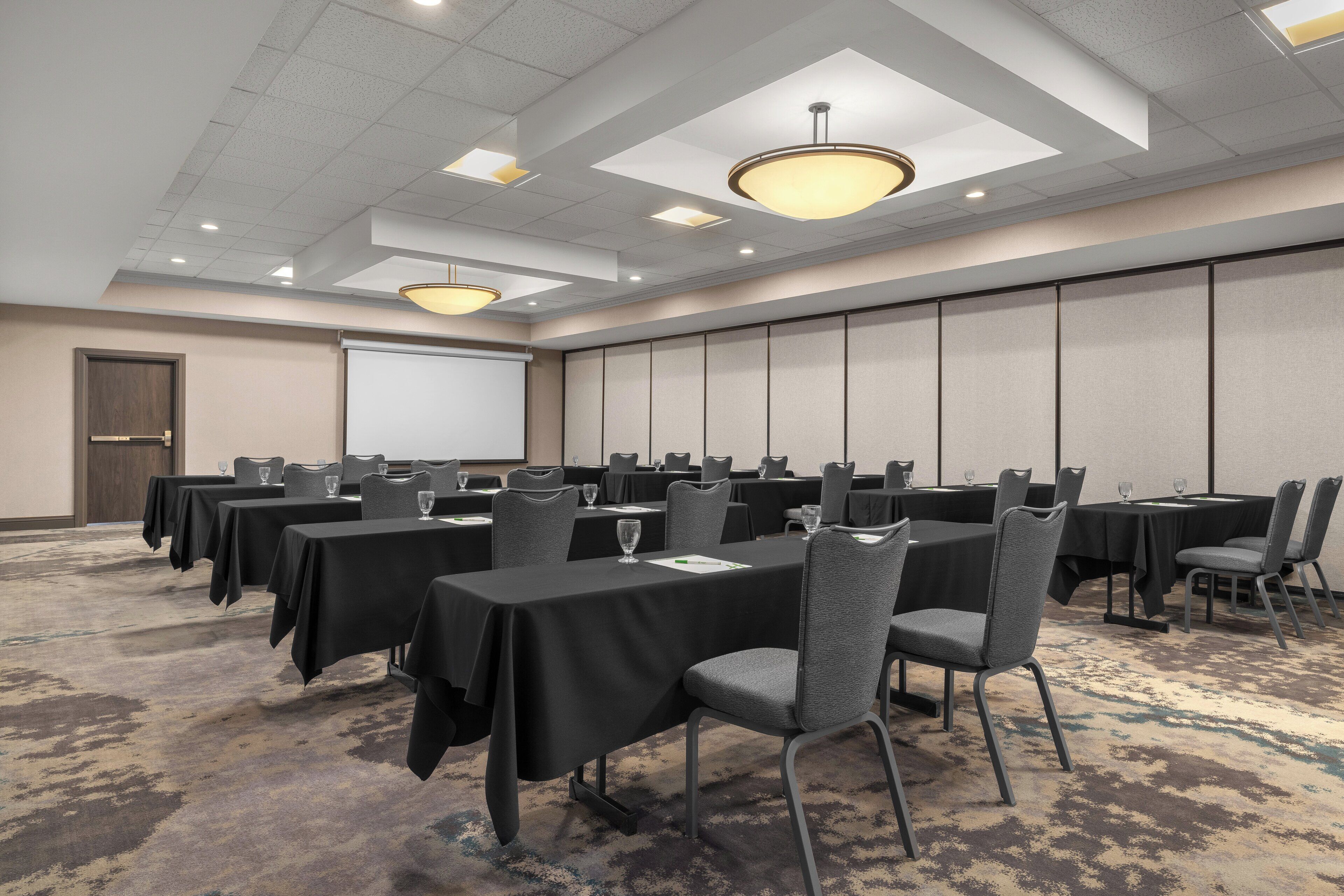 A conference room with multiple tables, chairs, and a projector screen.