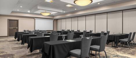 A conference room with multiple tables, chairs, and a projector screen.