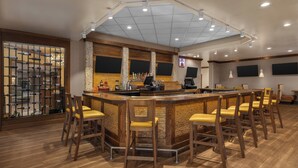 A bar area with a wooden bar counter, multiple stools, and a ceiling with recessed lighting. - Holiday Inn Dubuque/Galena by IHG (Dubuque)