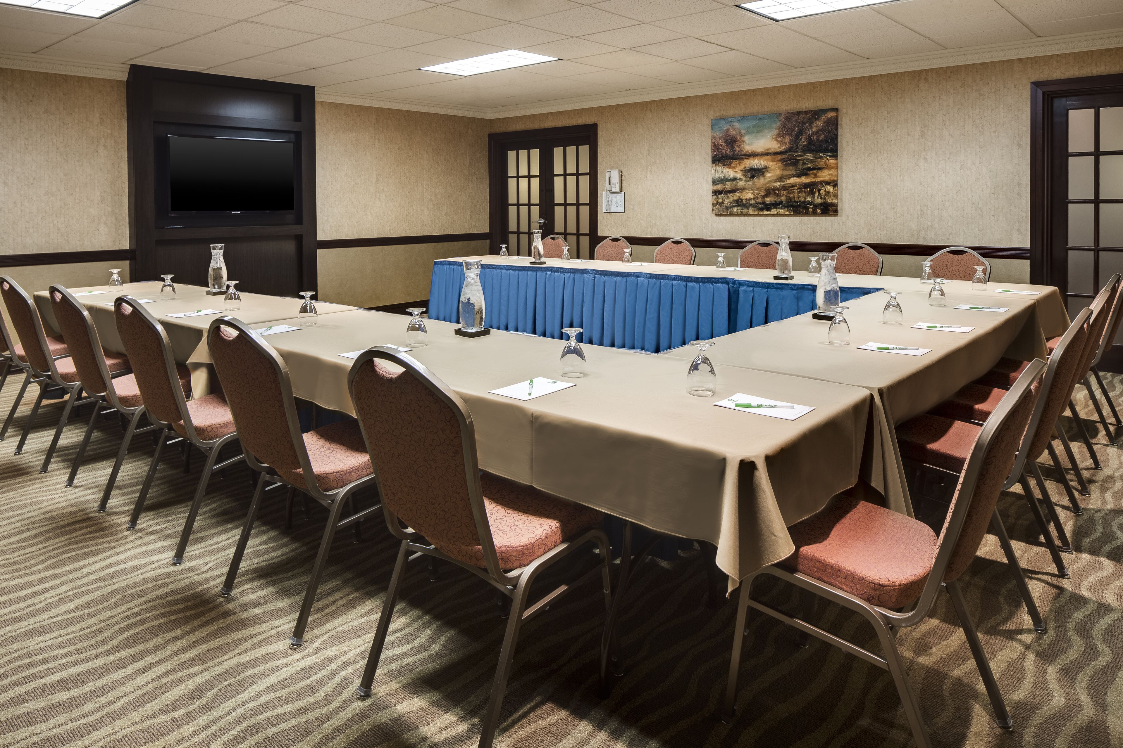 Un salón de conferencias con una larga mesa, sillas, un atril y una pantalla de televisión.