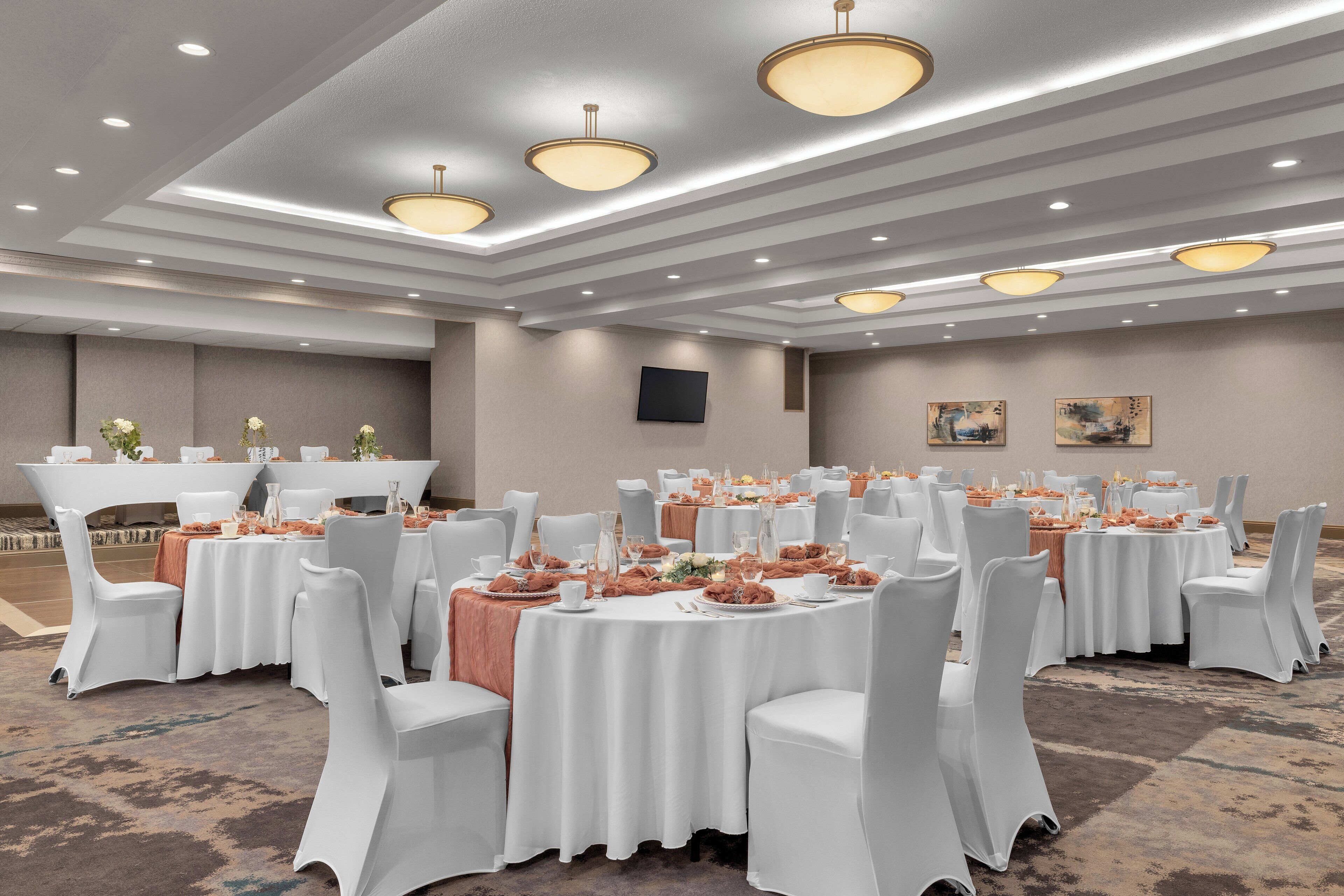 A banquet hall with round tables, white chairs, and overhead lighting.