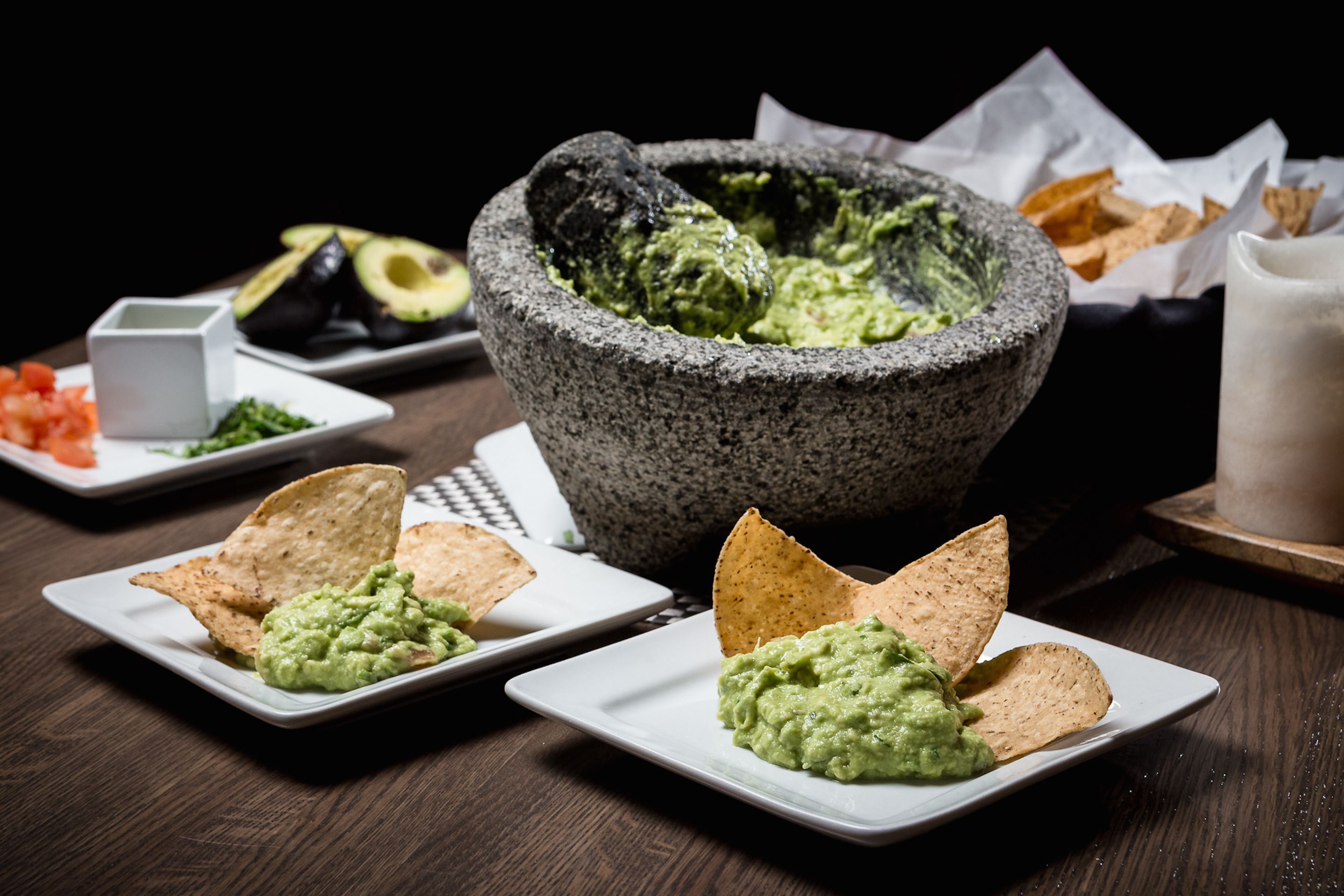 Pöydällä on kivinen mortteli, jossa on guacamolesalsaa ja tortilla-lastuja.