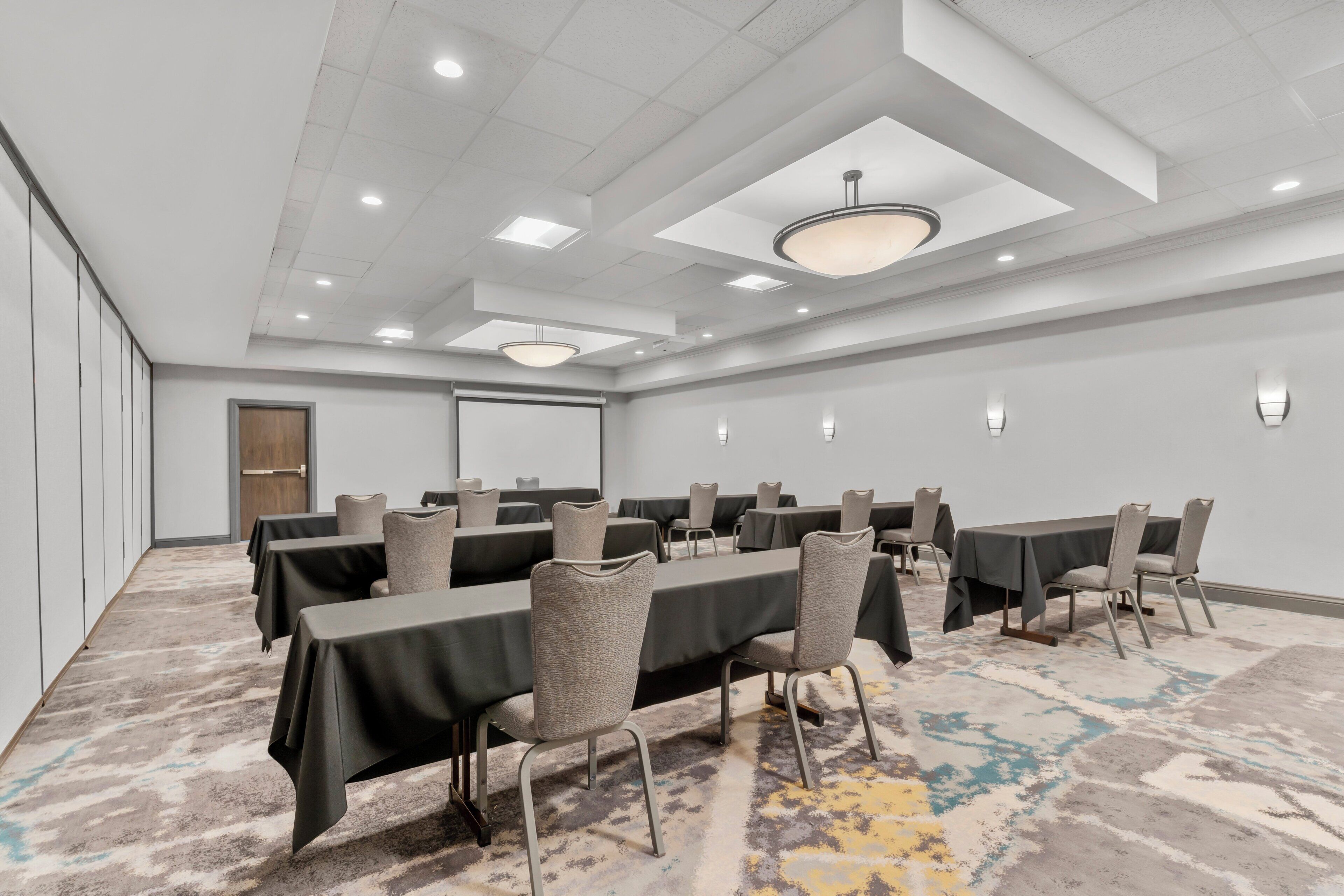 A conference room with tables and chairs, a projector screen, and a carpeted floor.