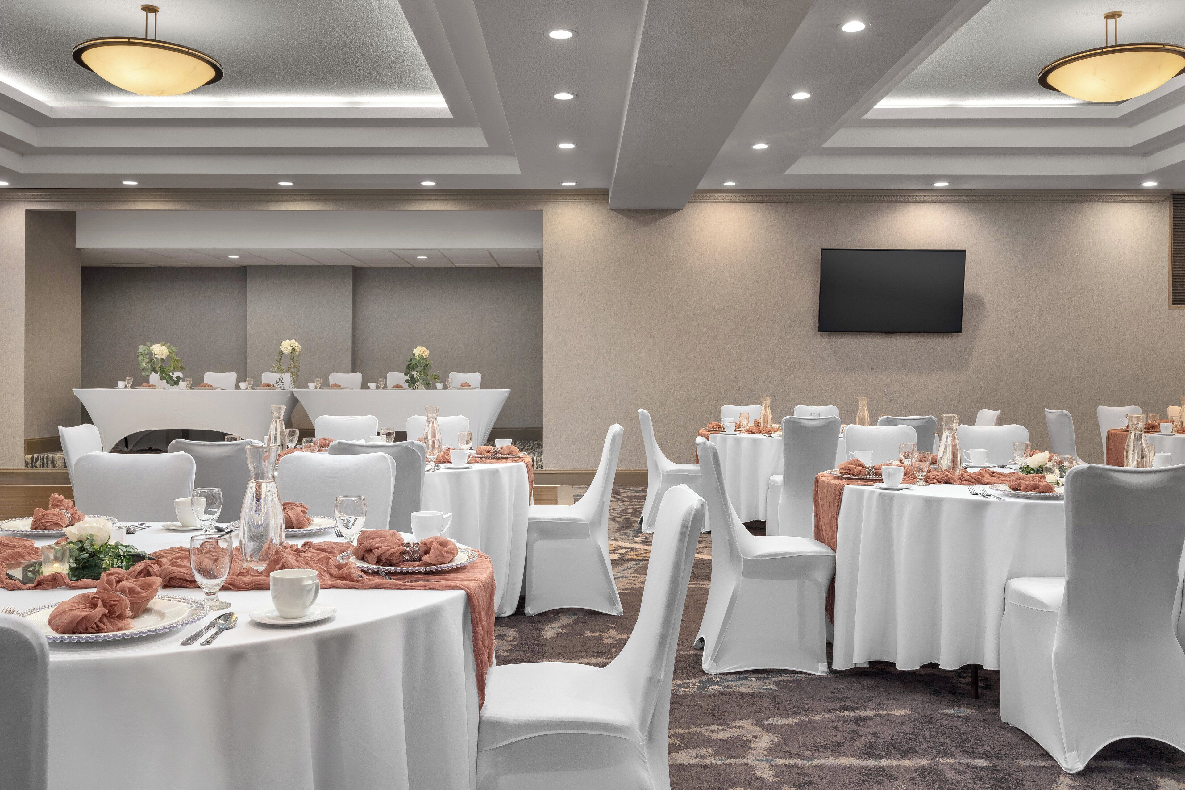 A conference room with round tables, white chairs, and a flat-screen TV on the wall.