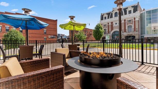 An outdoor seating area with wicker furniture and a fire pit, overlooking a street with buildings and a large glass structure. - Holiday Inn Dubuque/Galena by IHG (Dubuque)